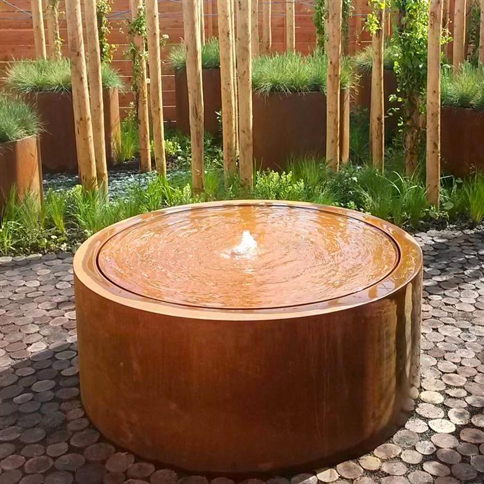 Der runde Wassertisch aus Cortenstahl ist wetterfest und langlebig. LED-Licht und Springbrunnen schaffen ein einzigartiges Ambiente, ideal für Garten oder Terrasse.
