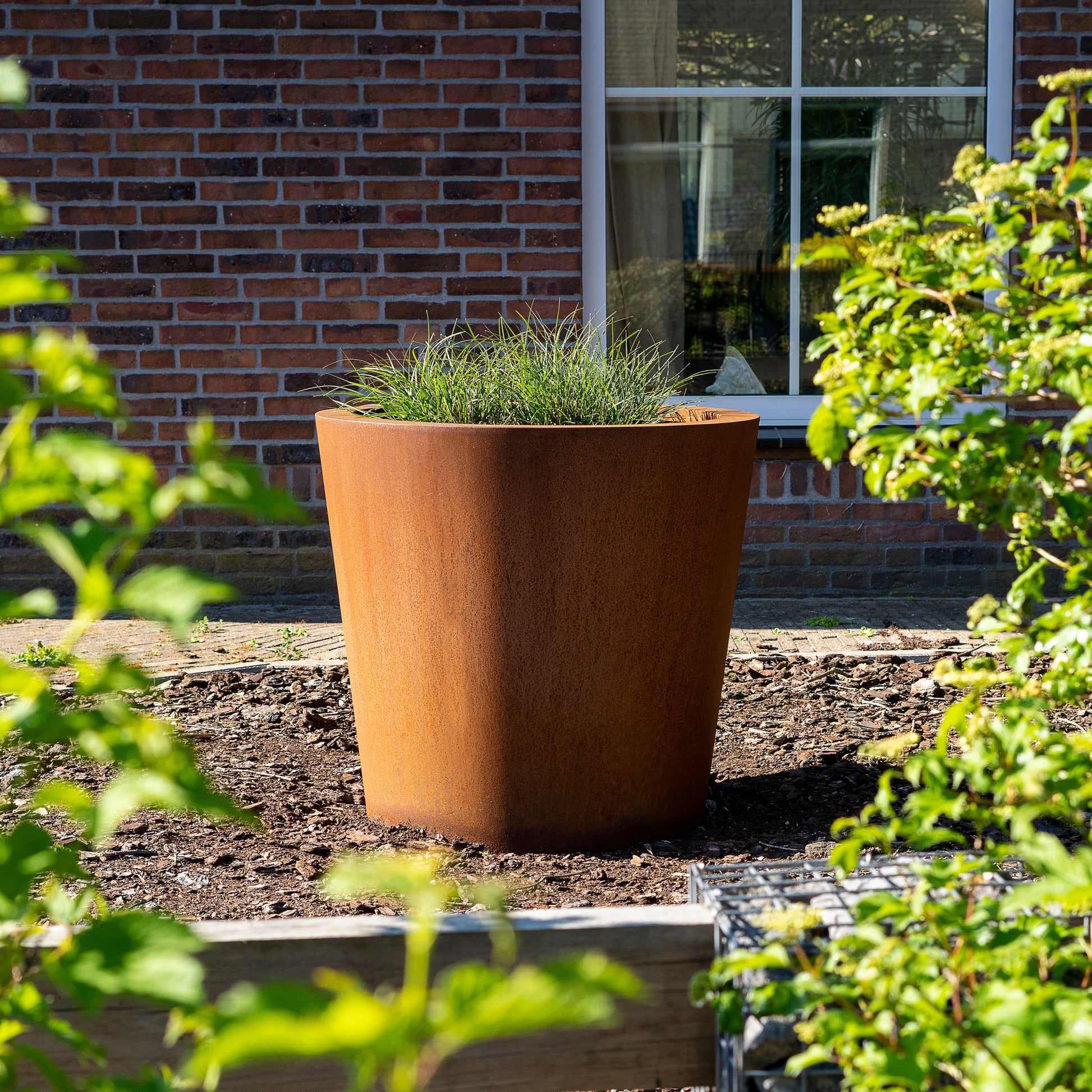 Das CONIC Pflanzgefäß aus Cortenstahl ist ein elegantes, wetterfestes Gefäß, das eine natürliche Rostschicht bildet, um den Außenbereich zu verschönern. Es hat eine stabile Basis mit Stützfüßen und Entwässerungslöchern, die für eine gute Pflege und lange Lebensdauer sorgen. Ideal für den Garten oder Park.