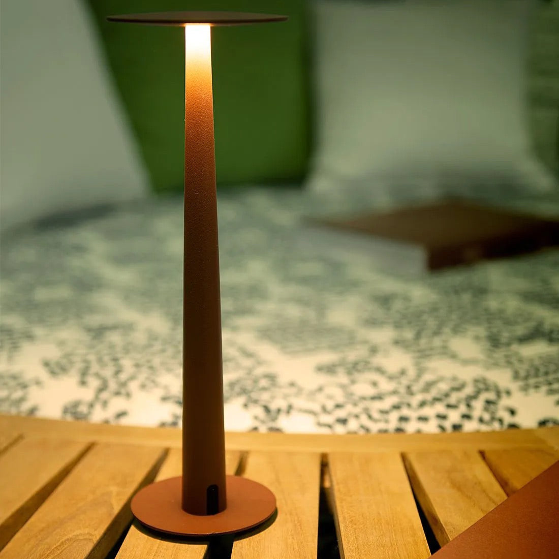 Portofino LED-Tischlampe in einem eleganten Outdoor-Setting, leuchtend auf einem Holztisch bei Abenddämmerung, schafft gemütliches Ambiente auf Balkon oder Terrasse.