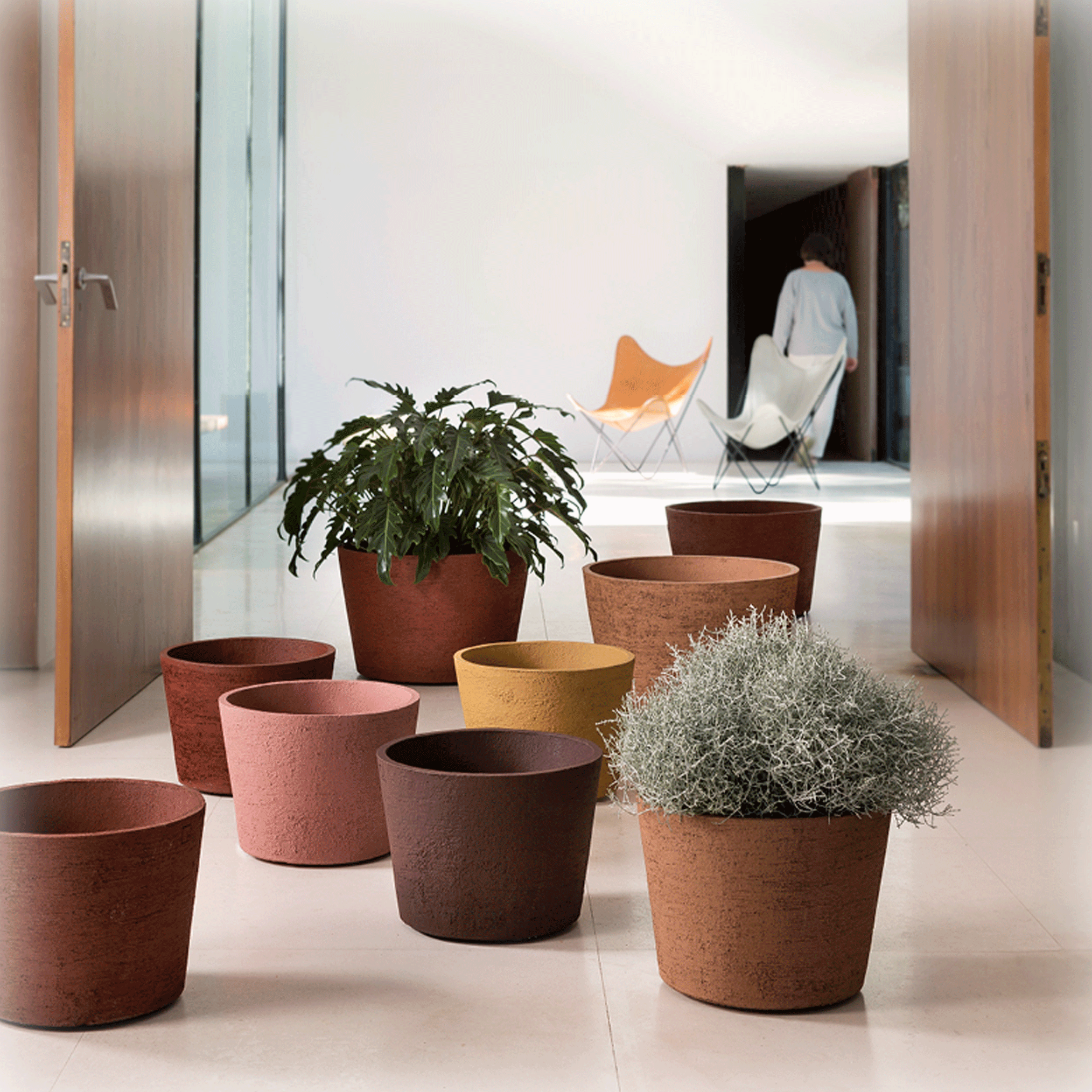 Neun Blumentöpfe vom Model MRB, stehen in unterschiedlichen Farben in einem hellen Flur. Die frostfesten Atelier Vierkant Gefäße eignen sich für den Wohnbereich sowie für kleinere Balkon. 
