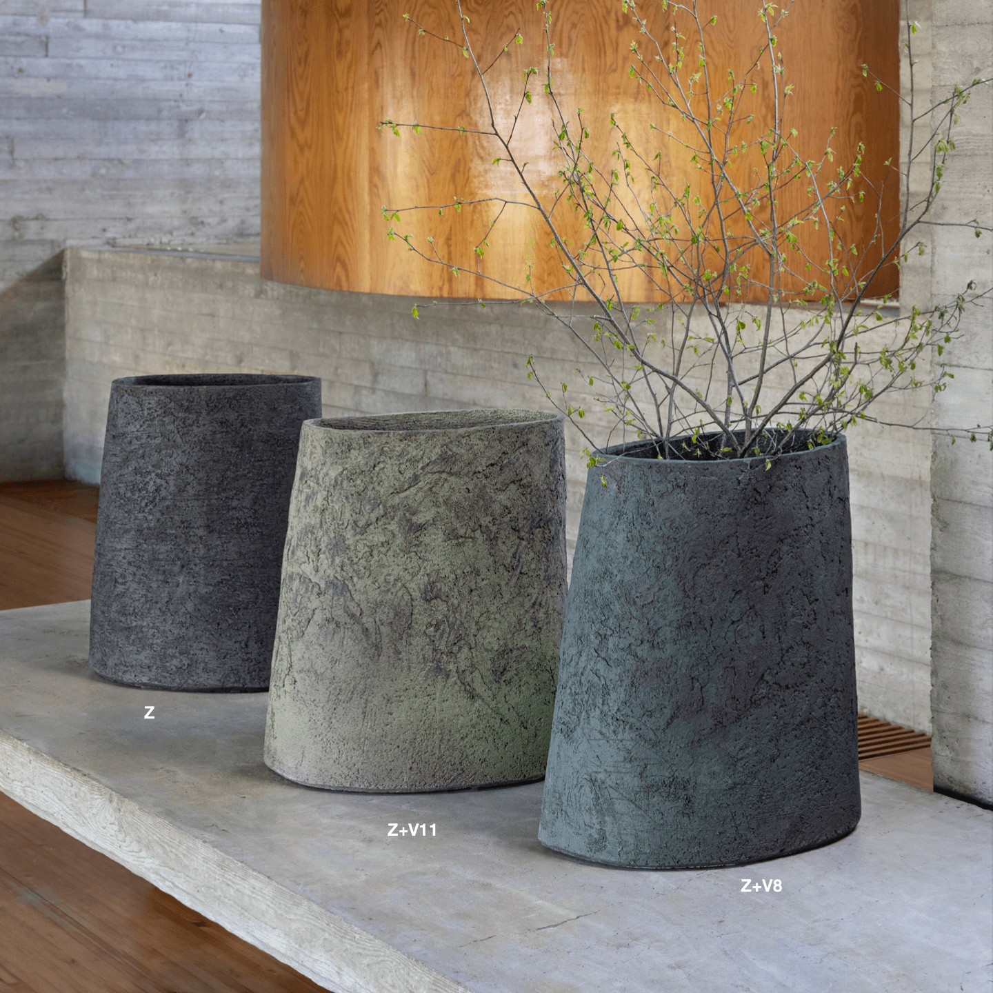 Drei Atelier Vierkant Vasen CCL50 stehen auf einem  Betonsockel. Die Gefäße sind von Links aus in schwarz, grün und blau.