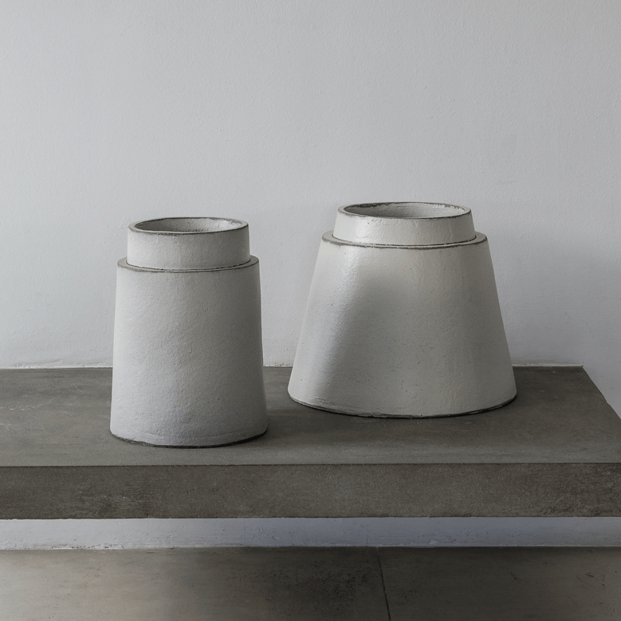 Auf einem Beton Regal stehen zwei glasierte weiße Gefäße von Atelier Vierkant. Die runden Gefäße GR und GRS40 sind aus Ton mit einer Höhe von ca. 36 cm.