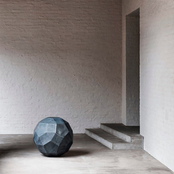 Domani Ornaments Ball besteht aus Zink und befindet sich in einem leicht dunklem Raum vor zwei grauen Stufen.