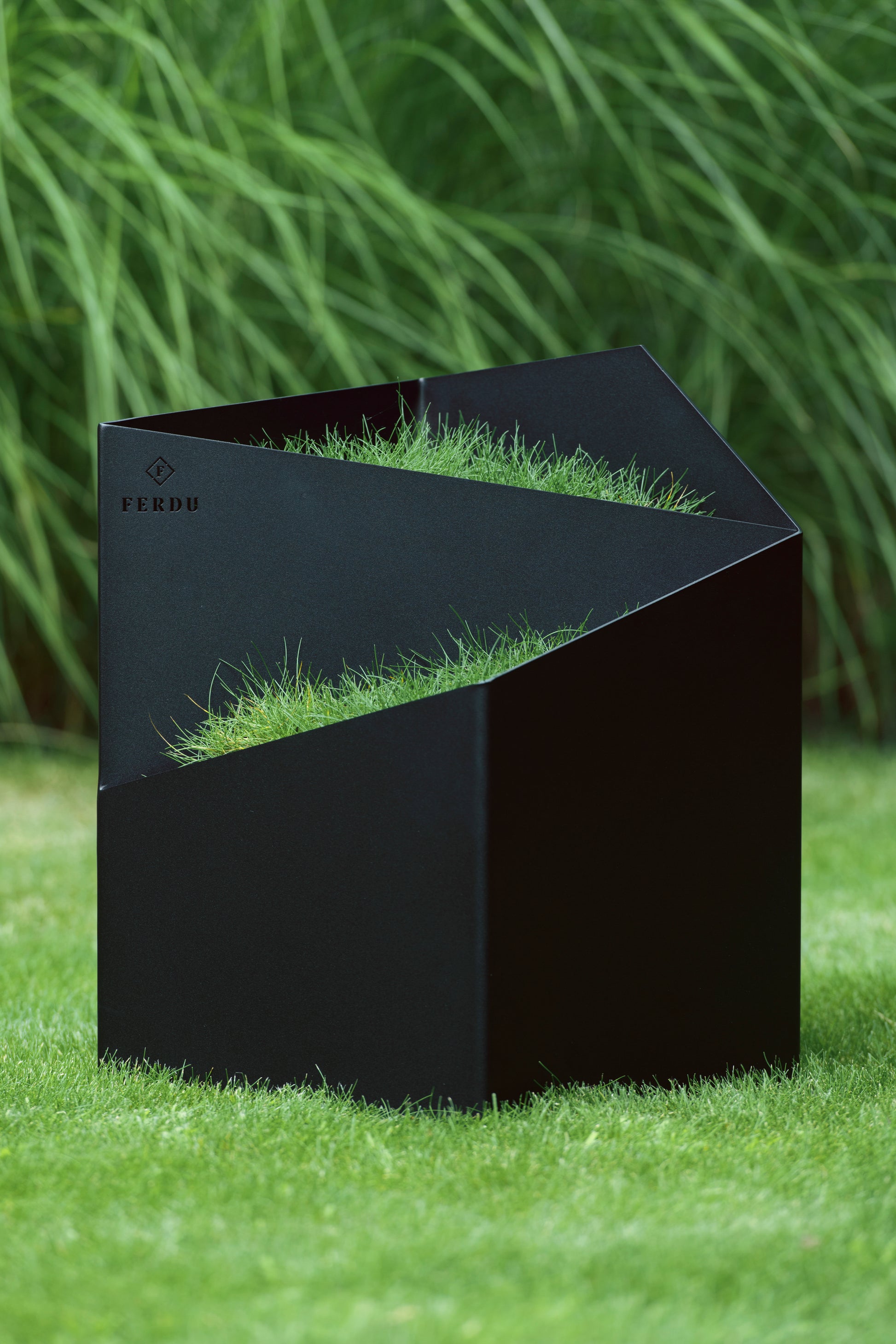 FERDU Gefaess Doblu aus CORTENSTAHL schwarz lackiert auf einem Rasen. Im Hintergrund sind Gräser gepflanzt.