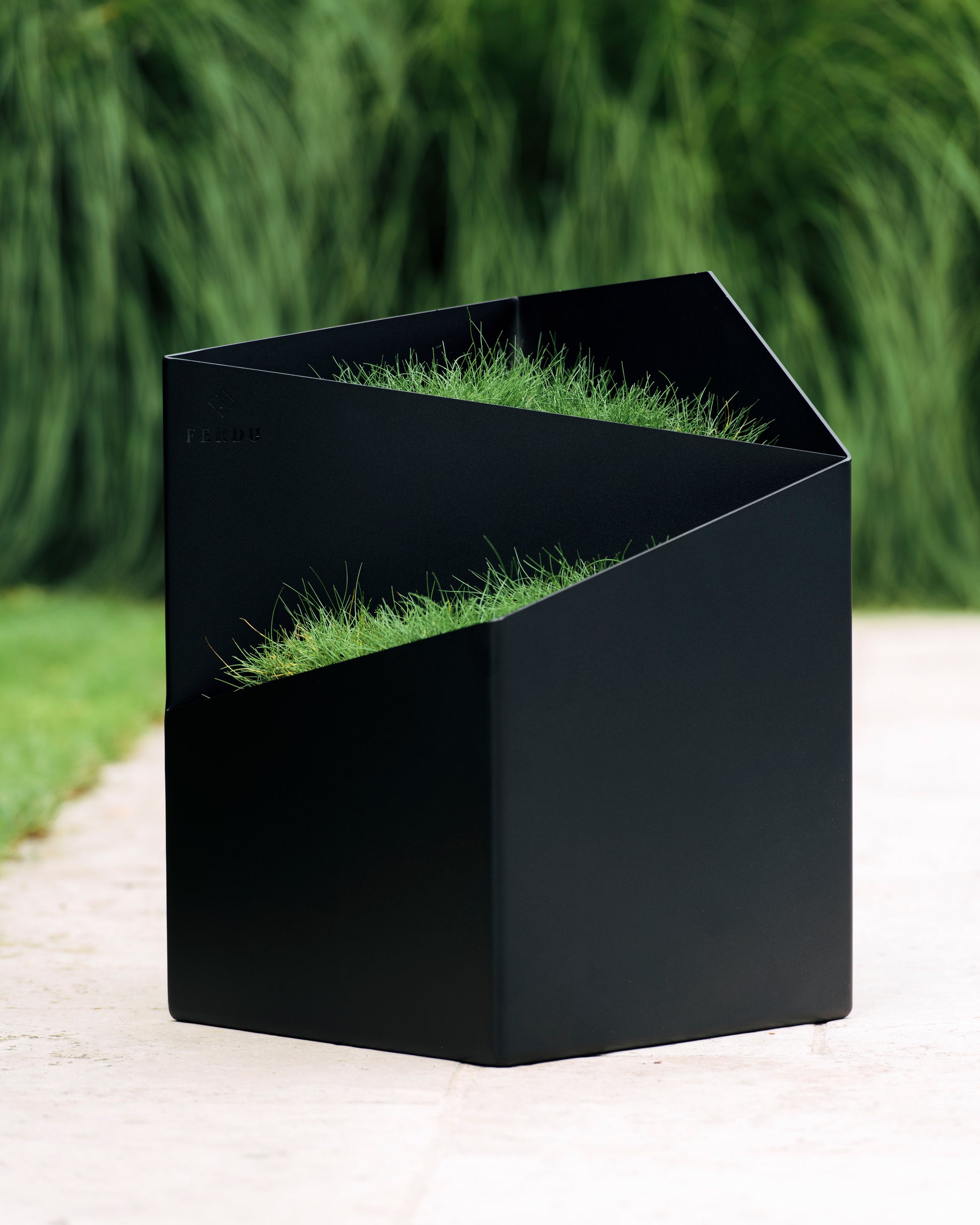 FERDU Gefaess Doblu aus CORTENSTAHL schwarz lackiert auf einer Terrasse. Im Hintergrund sind Gräser gepflanzt.