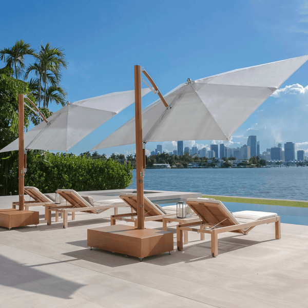 Auf einer Terrasse mit einem Blick auf Miami stehen zwei Tuuci Cantilever Sonnenschirme in Teak Finish. Unter diesen Luxus Sonnenschirmen stehen 4 Tribu Sonnenliegen aus Teakholz mit weißen Polstern.