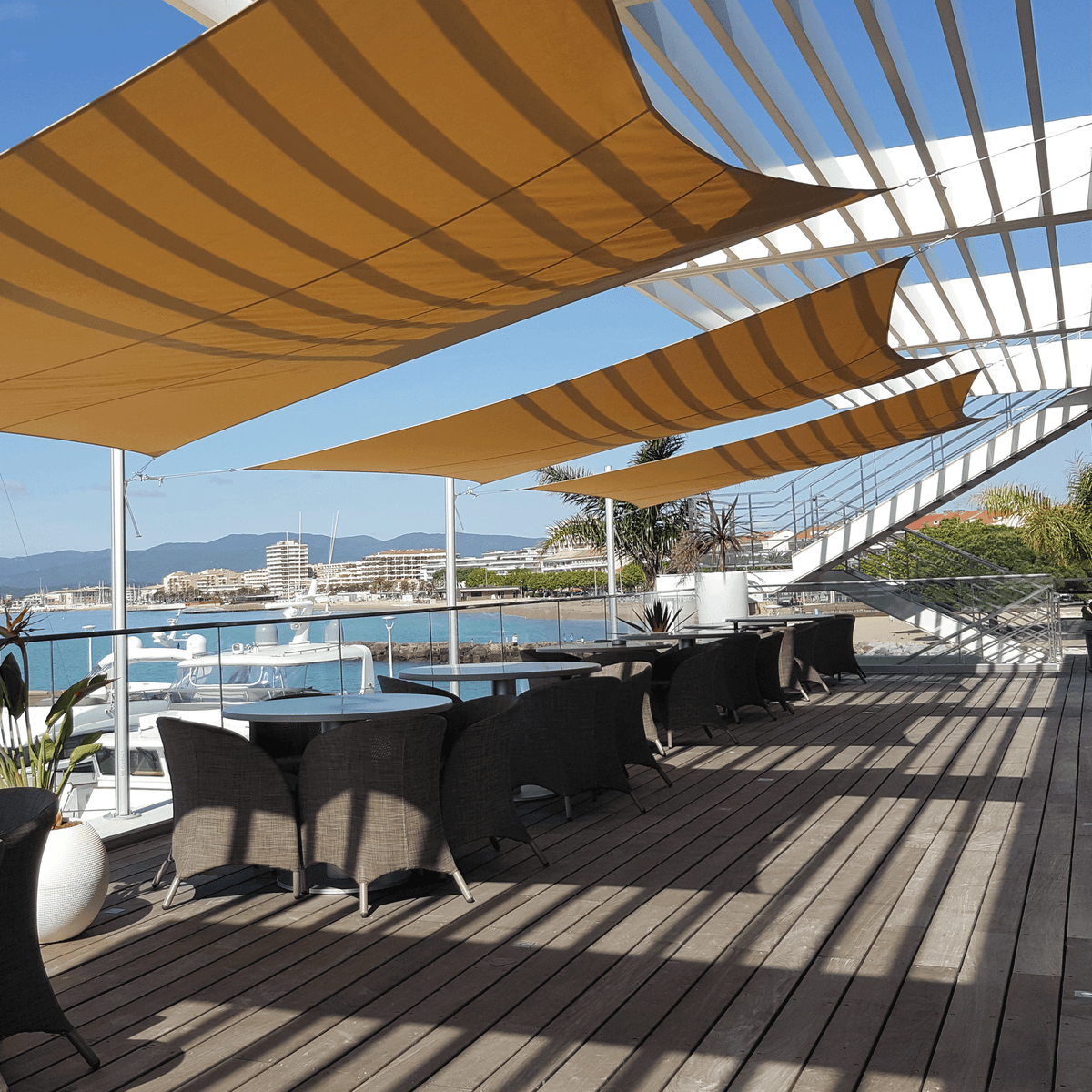 Gelbe Inngenua Sonnensegel dienen als Sonnenschutz für eine Terrasse eines Kaffee´s am Meer.