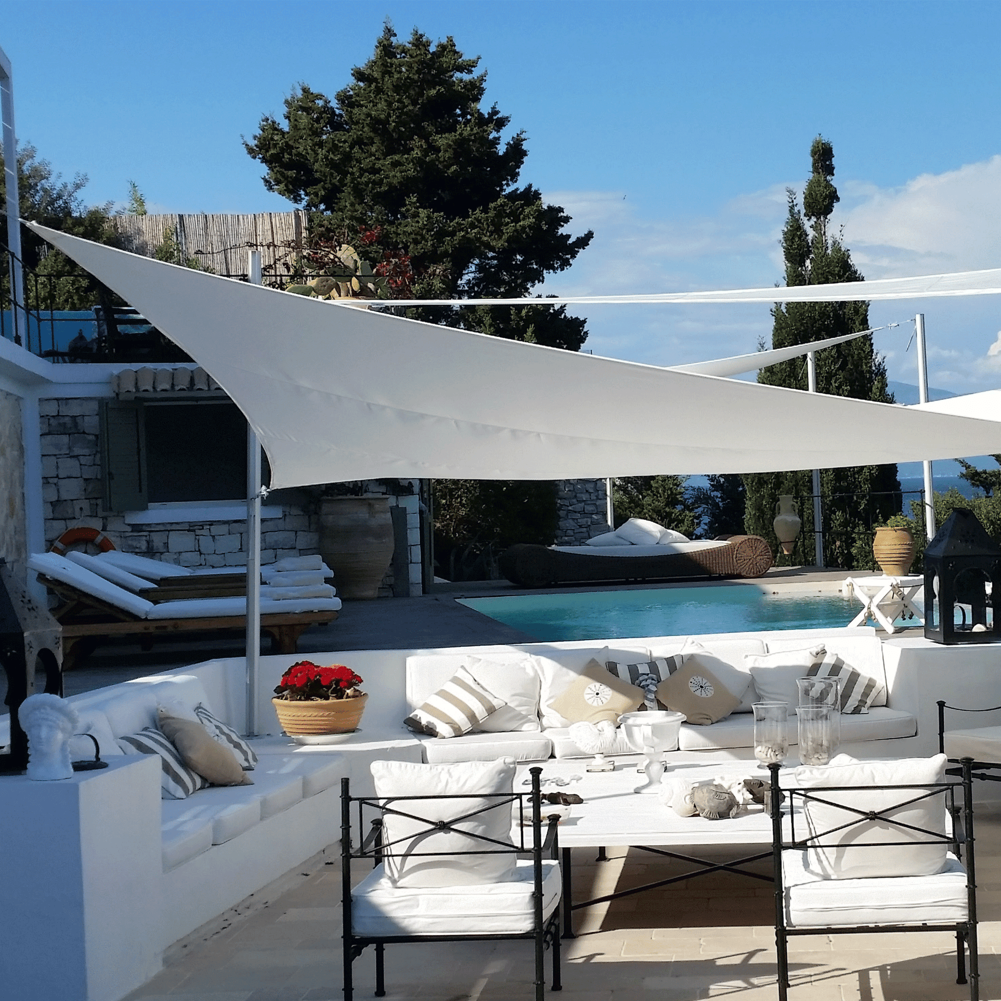 Umbrosa Sonnesegel in weiß 4x4x4m. Das Segel dient zur Beschattung einer Lounge aus Gusseisen.