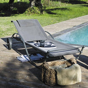 Unopiu Liege Aurora in grafitgrau mit brauner Bespannung. Auf der Sonnenliege liegt ein Katalog und ein Wasserglas.