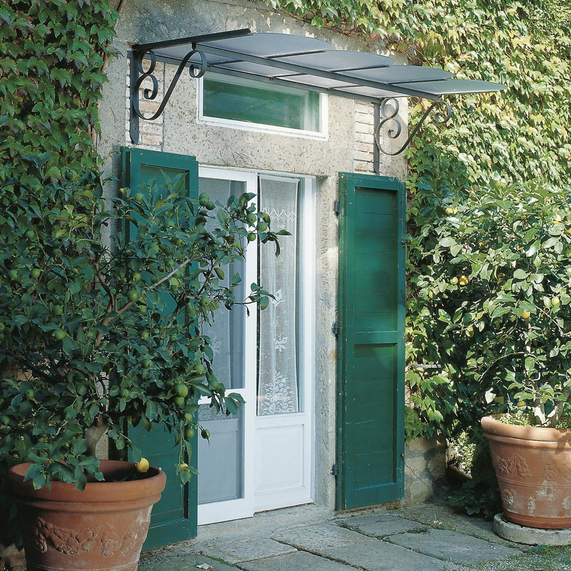 Das Unopiu Vordach Dafne besteht aus verzinktem Eisen und ist grafitgrau pulverbeschichtet. Es schützt durch eine Abdeckung aus strukturiertem Polycarbonat zuverlässig vor Regen und Schnee.