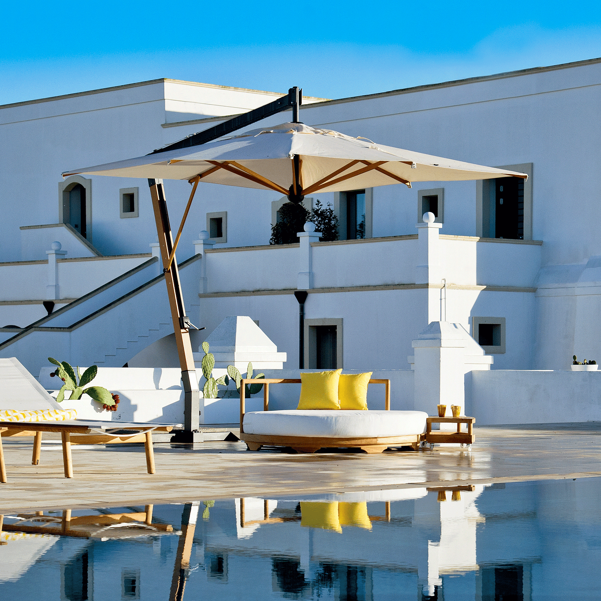 Unopiu Daybed dekoriert mit 2 gelben Kissen in der Größe von 40x40cm. Die Insel steht an einem Pool vor einer alten weißen italienischen Villa.