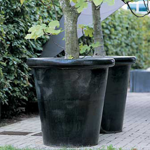 Zwei sehr schöne Domani Pflanzgefäße aus der Kollektion London stehen vor einer großen grünen Hecke in einem Londoner Innenhof. Die schwarzen Tröge haben einen Ø78cm und eine Höhe von 78cm. Diese sehr schönen Blumenkübel sind Frostbeständig.