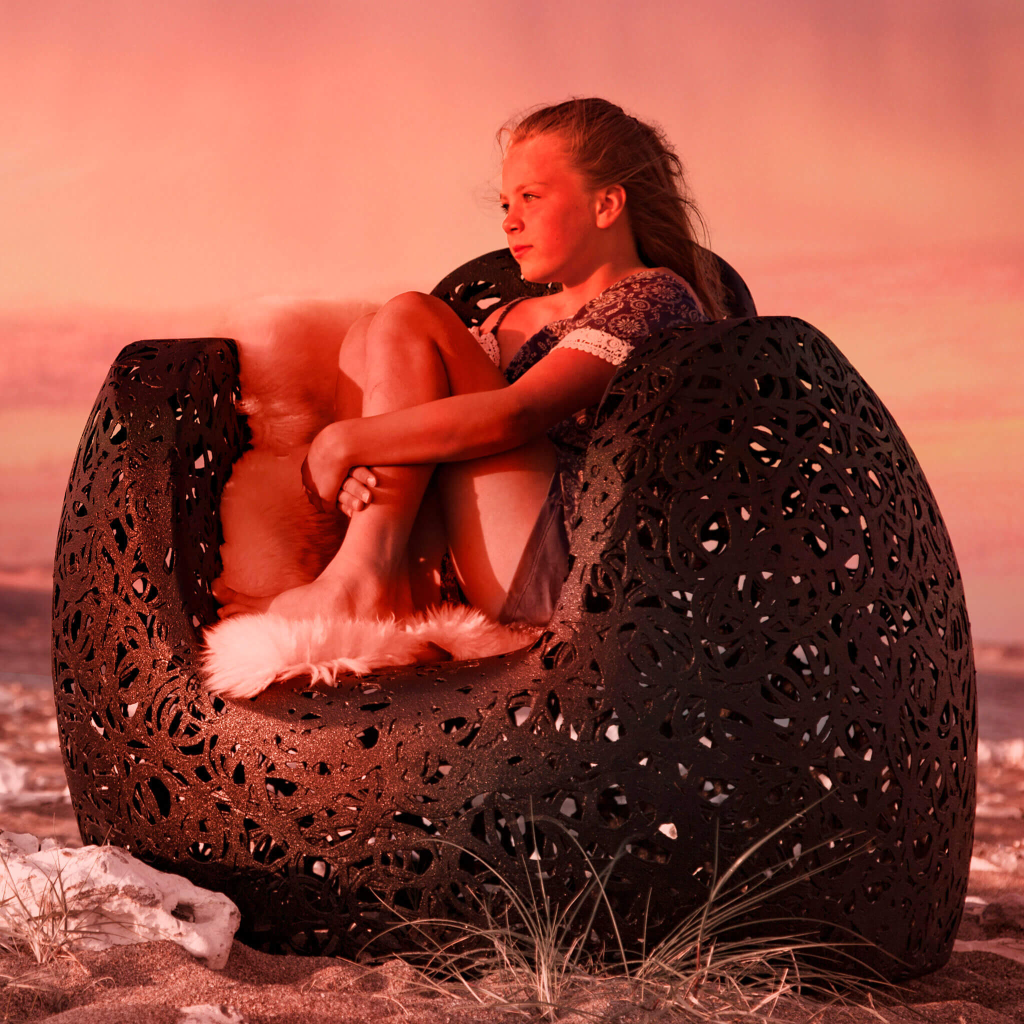 Am Strand steht ein schwarzer Unknown Nordic Stellar Chair. In dem sehr schönen Lounge Sessel sitz ein Kind auf einem Fell