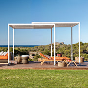 weiße Unopiu bewegliche Pergola Shibuya auf Rollen. Unter der Pergola stehen 2 Synthesis Liegen aus Teakholz mit orangenen Auflagen.